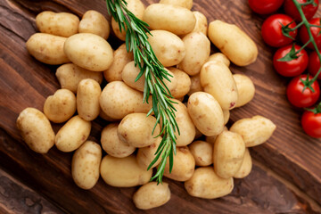 Raw young small potato with rosemary and cherry tomatoes on wooden background