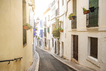 view of small street with white houses and flowers in the traditional spanish town of Sitges in the Catalonia region