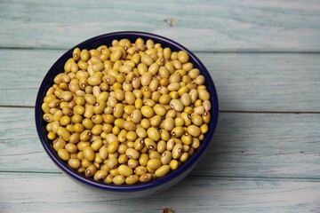 Yellow Ball Beans (Phaseolus vulgaris) in a blue bowl, isolated, on a wooden table, top view.