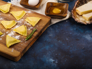 Cooking homemade ravioli. Raw ravioli on a cutting board with a sprig of rosemary. Kitchen utensils, ingredients on a blue marble background. Recipes for classic Italian ravioli.