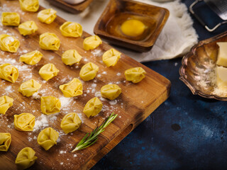 Cooking classic homemade dumplings, ravioli. Small dumplings, ravioli on a wooden cutting board with a sprig of fragrant rosemary. Ingredients, kitchen utensils. Food background.