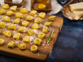 Homemade raw ravioli on a cutting board with a sprig of rosemary on a marble background. Recipes for home and restaurant cuisine. Recipe book, food blog. Advertising, banner.