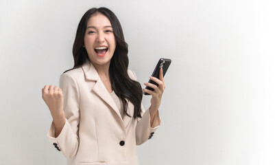 Surprised young Asia lady using mobile phone with positive expression, smiles broadly, dressed in casual clothing and looking at camera on white background. Happy adorable glad woman rejoices success.