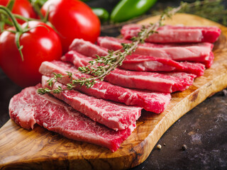 Close-up. Appetizing meat steaks with a sprig of rosemary on a cutting board are waiting to be cooked. Fresh vegetables on a dark background. Picnic, banquet.