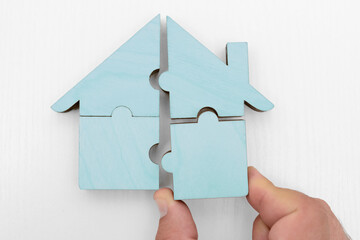 male hand holds pieces of blue wooden house puzzle isolated on white  background. wooden home made...