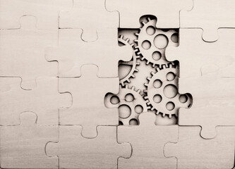 solving the problem concept - puzzles and cogwheels. wooden gears under the puzzle, the concept of moving to the next level. Cog wheels coming out from underneath a jigsaw puzzle.