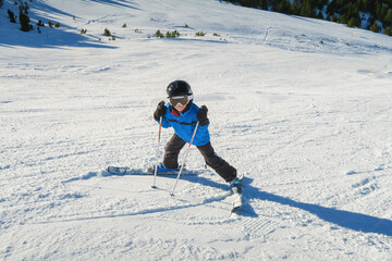 a little beginner skier on a ski slope in a funny inverted position and smiling behind the goggles...