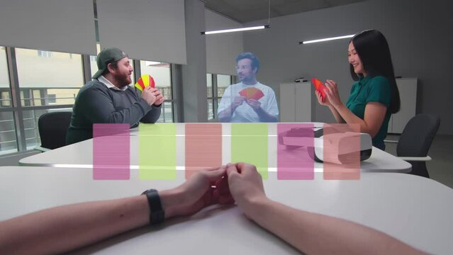 People in casual clothes sit at table in startup office and play virtual card game with colleague avatar