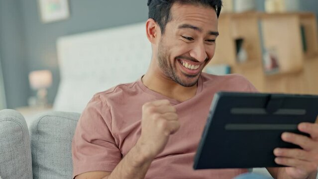 Man on a digital tablet winning a game online while sitting on a sofa in his living room at home. Happy and excited guy celebrating the victory of successful sport bet on the internet with technology