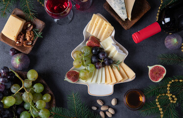 Variety of cheese and fruits served in plate as Christmas tree, on dark gray background with two glasses of wine. New Year's Eve Party Snack. Top view