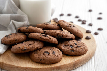 Homemade chocolate chip cookies on wooden board with glass of milk and kitchen towel. Recipe of traditional pastry for tea, freshly baked cookies with pieces of chocolate.