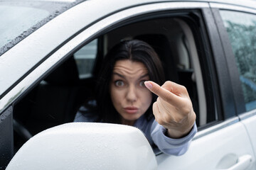 Aggressive woman driving car. Negative human expression with Forefinger, come here gesture with hand. Drivers and pedestrians conflict on street roads on rainy day. Drops on a wet car. Selective focus