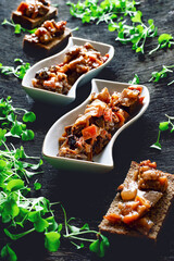 Appetizer of fried eggplant with prunes in unusual plates, a lot of microgreens scattered around, on a black textured background, delicious food