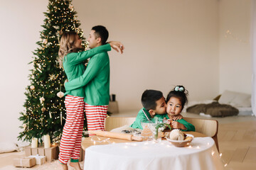 An Asian family with two children in green pajamas cook together festive cookies celebrate the Christmas holiday in a decorated house in winter. Mom dad son and daughter spend time together on vacatio