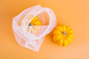 Happy Thanksgiving.Vegetable fall food concept.Autumn Halloween Pumpkins.Different varieties of Pumpkins in mesh bag of fabric on orange background.Autumn concept.Copy space.Composition of pumpkins.