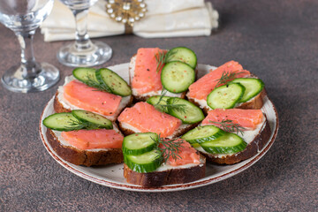 Sandwiches with salted salmon, cucumber and dill on bread on brown background. Festive snack