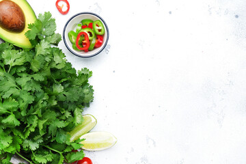 Fresh cilantro or coriander, chili and jalapeno peppers, avocado, lime and cherry tomatoes - ingredients for Mexican spicy cuisine. White kitchen table background, top view