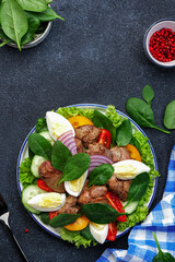 Perigord salad with chicken liver, tomatoes, cucumbers, eggs, lettuce and spinach. Black kitchen table background, top view