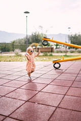Little girl walks along the rubber surface of the playground to the swing-balancer. High quality...