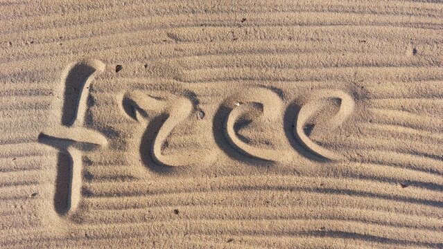 The word Free is written in the sand on the beach