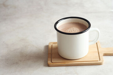 Hot cocoa in a white mug stands on a wooden stand on the table. Copy space