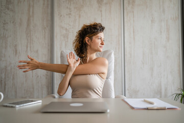 young woman stretching at work while sitting at desk having back pain