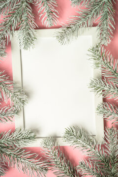 Christmas composition with photo frame and fir tree branch at pink background. Flat lay image with copy space.