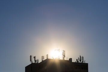 Many mobile transmitters on the roof of a high-rise building in the background with the sun