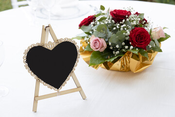Segnaposto a forma di cuore e bouquet di fiori su un tavolo coperto da una tovaglia bianca, primo piano