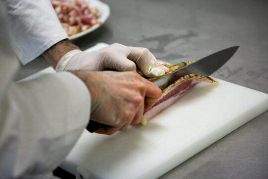 Uomo che taglia una fetta di pancetta, mani e coltello in primo piano