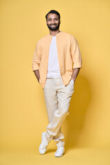 Fototapeta premium Smiling happy confident rich indian man standing isolated on yellow background. Happy handsome ethnic guy looking at camera advertising products posing for vertical full length portrait.
