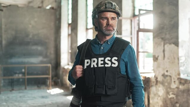 Camera approaching male war press correspondent with photo camera. Cameraman working for military news journal. Handsome man journalist in bulletproof vest and helmet in damaged facility