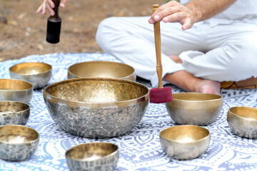 Close-up of man hands playing on a singing tibetian bowl with sticks. Sound healing music instruments for meditation, relaxation, yoga. Sound therapy. Buddhist healing practices.Selective focus