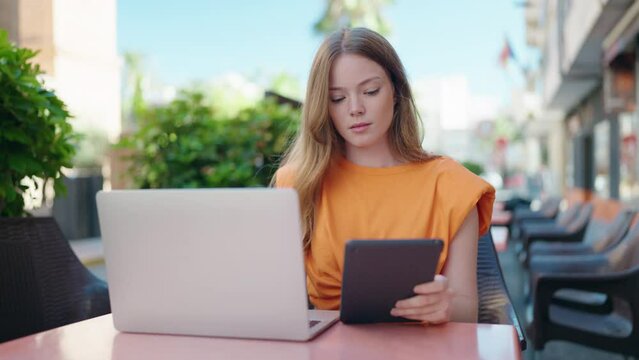 Young woman using laptop and touchpad sitting on table at coffee shop terrace