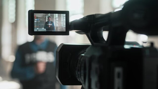 Close up shot of professional camera recording male journalist in bulletproof vest and helmet reporting live in damaged building. Behind the scenes of war. War press correspondent on camera screen