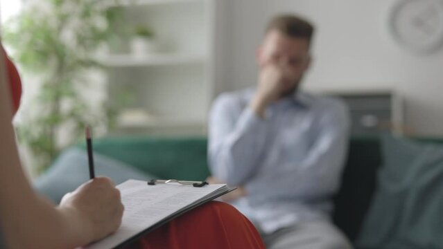 Woman medical doctor psychologist making notes while listening to male patient, mental healthcare concept