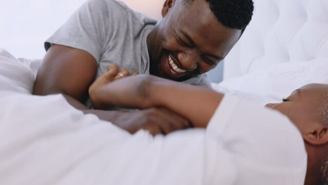 Happy playful black couple smile in bed at home and laugh together. Romantic man and woman bonding in their bedroom in the morning. Carefree boyfriend and girlfriend romance, funny and intimate