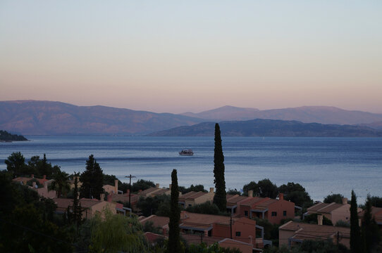 Barbati, Corfu, Greece. Beautiful pink sunset. Floating boat. Mountains in the haze. Holidays in Greece.