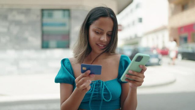 Young hispanic woman using smartphone and credit card at street