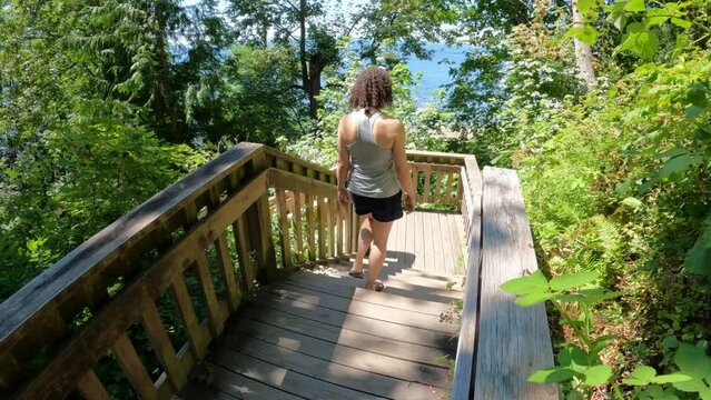 Woman Hiking Wooden Trail in the green forest with trees during sunny summer day. 1001 Steps in White Rock, Greater Vancouver, British Columbia, Canada.