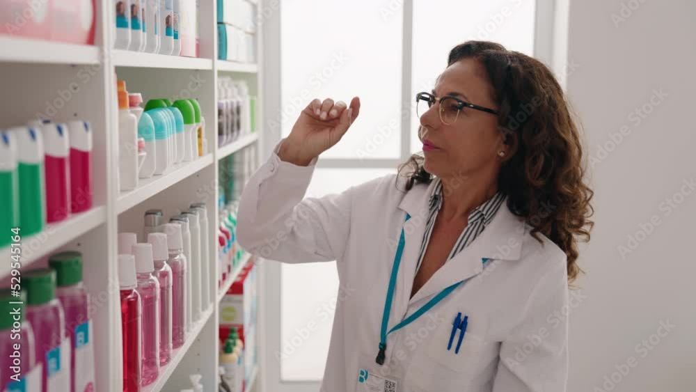 Wall mural Middle age woman pharmacist holding sunscreen bottle at pharmacy