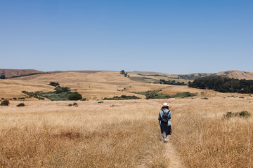 Fototapeta na wymiar Woman in a hat walking outdoors through the hills with dry grass, view from the back
