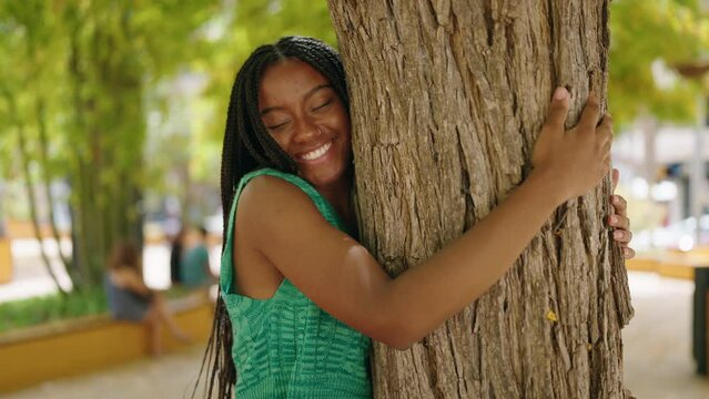 African american woman smiling confident hugging tree at park