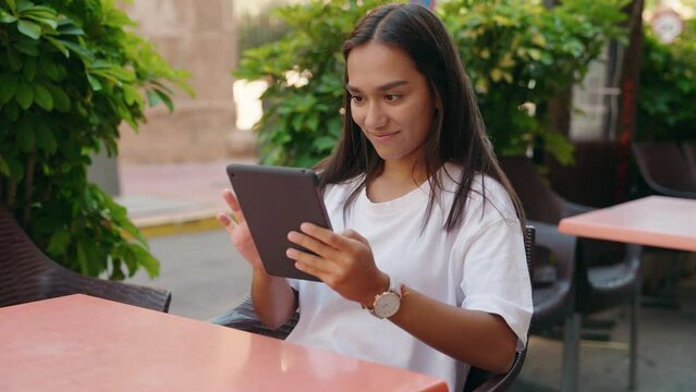 Young beautiful hispanic woman using touchpad sitting on table at coffee shop terrace