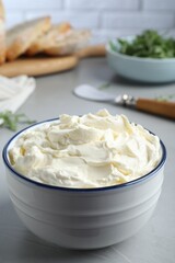 Bowl of tasty cream cheese on grey table