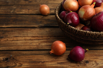 Onion bulbs and basket on wooden table. Space for text