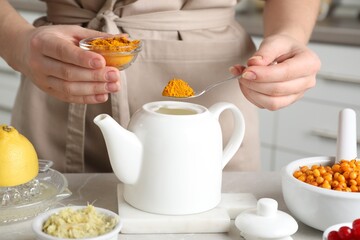 Woman making immunity boosting drink with turmeric powder at marble table, closeup