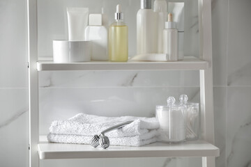 Metal face roller, towels and cosmetic products on shelving unit in bathroom