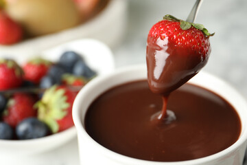 Dipping strawberry into fondue pot with chocolate, closeup