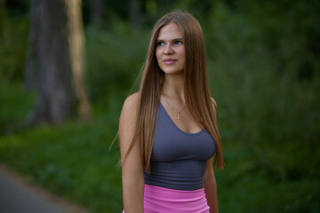 Lovely young woman with sexy boobs in trendy gray top in pink fashionable sports shorts walking on street. Pretty beauty girl fashion model walks in park. Healthy lifestyle.
